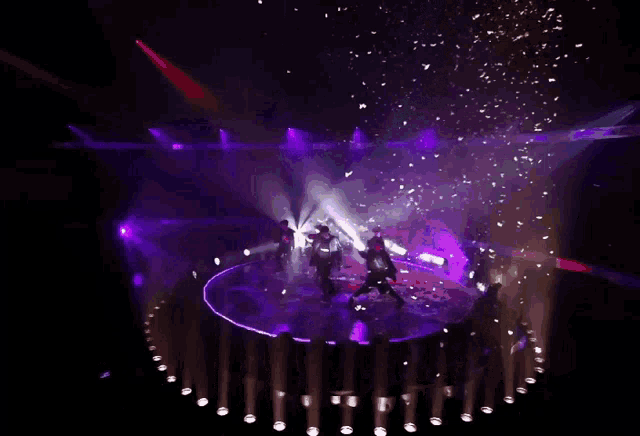 a group of people are dancing on a stage in front of purple lights