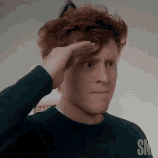 a man with red hair is wearing a black sweater with the letters snl on the bottom