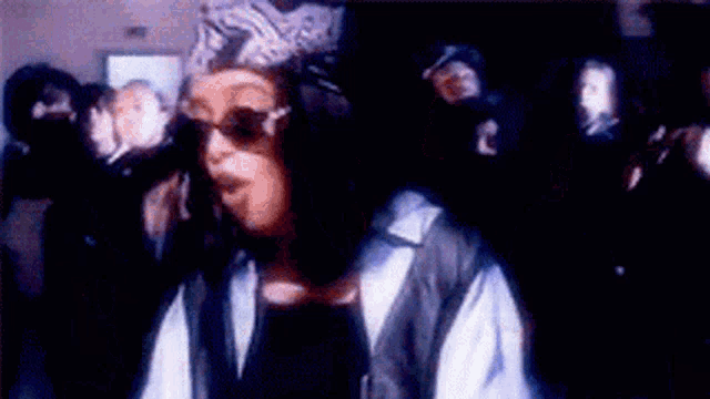 a man wearing a helmet and sunglasses is dancing in a dark room with a group of people .