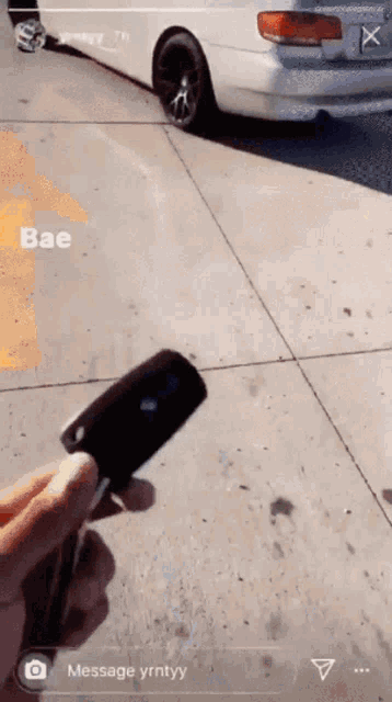 a person is holding a car key in front of a white car with the word bae on the sidewalk