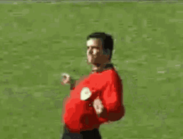 a man in a red shirt is standing on a soccer field with his arms outstretched