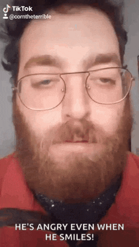 a man with a beard wearing glasses and a red shirt is smiling .
