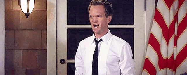 a man in a white shirt and tie is standing in front of a door and shouting .