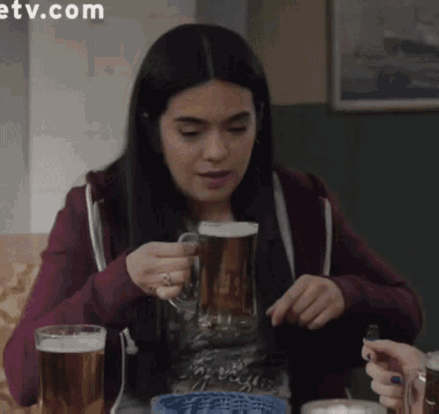a woman sitting at a table with a mug of beer in her hand