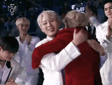 a man in a red jacket is hugging another man in white