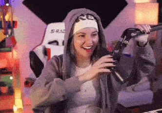 a woman wearing a headband and a hoodie is holding a microphone and smiling .
