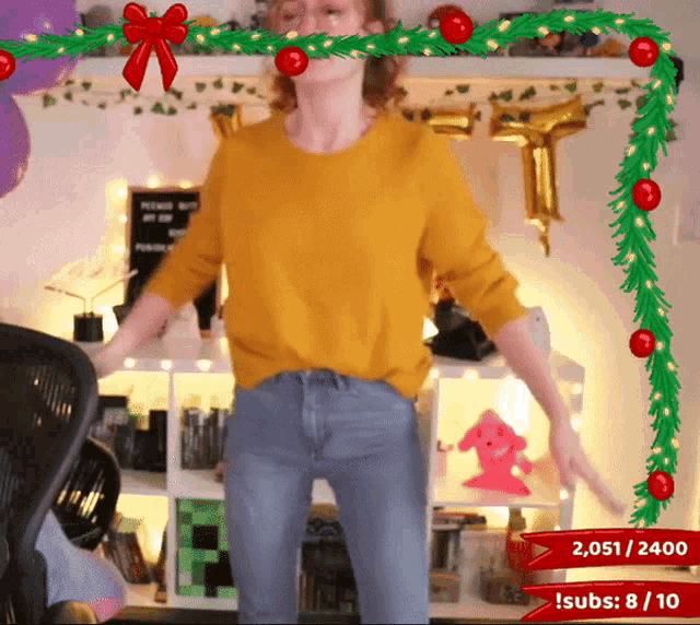 a woman in a yellow sweater is dancing in front of a christmas decoration that says 2,051/2400