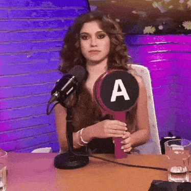 a woman sitting in front of a microphone holding a circle with the letter a on it