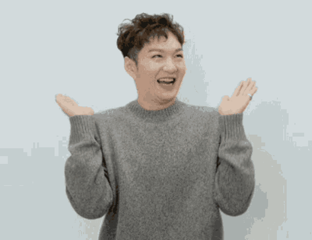 a man wearing a grey sweater is laughing with his hands in the air