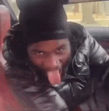 a man in a black hat is sticking his tongue out while sitting in a car .