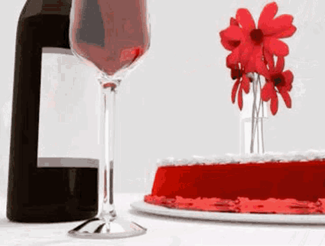 a bottle of wine a glass of wine and a red cake on a table