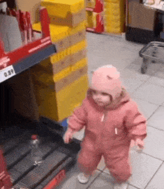 a baby in a pink jumpsuit is walking in a store .