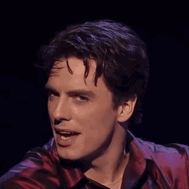 a man in a red shirt is smiling on a stage in front of a black background .