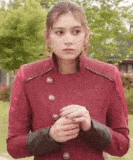 a woman wearing a red jacket with black sleeves is standing in a park .