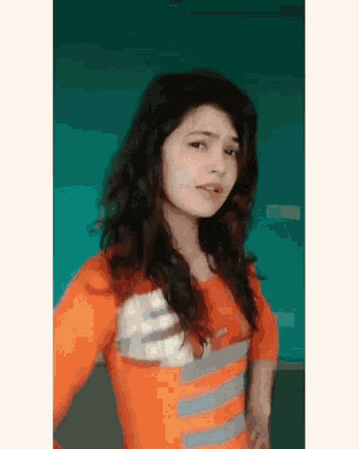 a young woman wearing an orange nike shirt stands in front of a blue wall