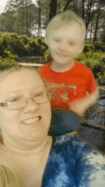 a woman wearing glasses and a red shirt is holding a young boy