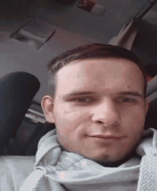 a man is sitting in a car with a scarf around his neck and smiling .