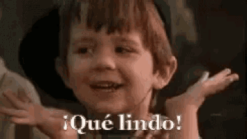 a young boy is making a funny face with his hands outstretched and the words `` que lindo '' written on the bottom .