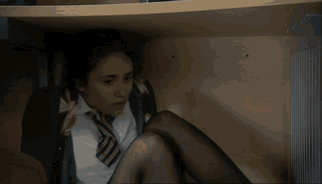 a girl in a school uniform and tie is looking under a shelf