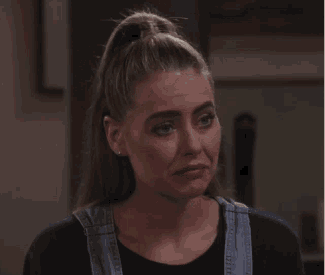 a woman wearing overalls and a ponytail looks sad