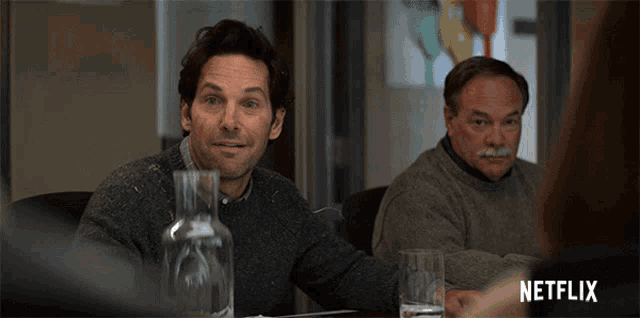two men are sitting at a table with a bottle of water and a netflix logo