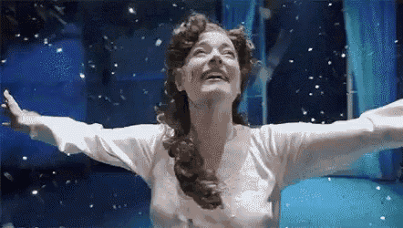 a woman is standing in front of a window with her arms outstretched and snow falling around her .