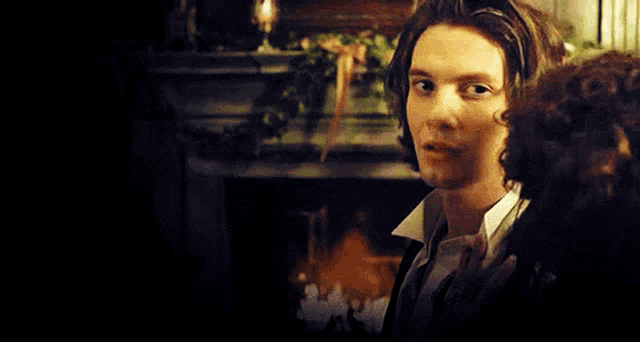 a man in a white shirt and suspenders looks at a woman in a dark room