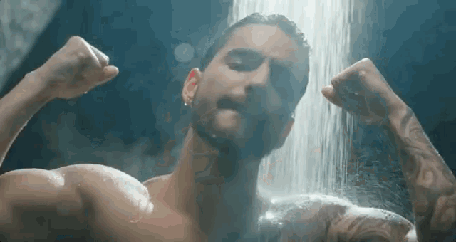 a shirtless man is flexing his muscles under a shower .