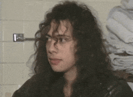 a man with long curly hair is standing in front of a wall with towels hanging on it .