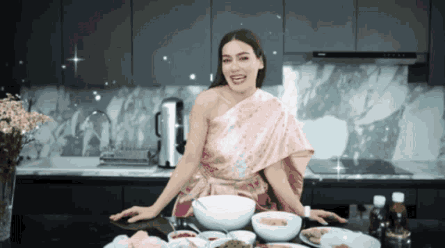 a woman in a pink dress is standing in a kitchen surrounded by bowls of food