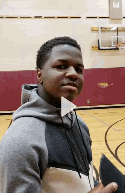 a young man standing on a basketball court looking at the camera with a play button on his neck