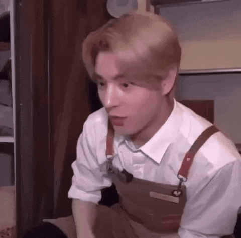 a man wearing a white shirt and an apron is sitting in a kitchen .