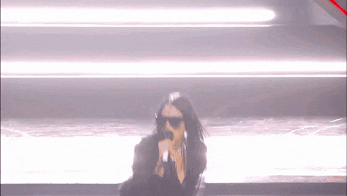 a woman wearing sunglasses is singing into a microphone on stage .