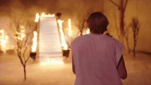 a woman is standing in front of a building that is on fire