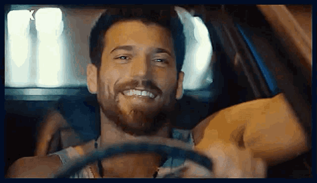 a man with a beard is driving a car and smiling