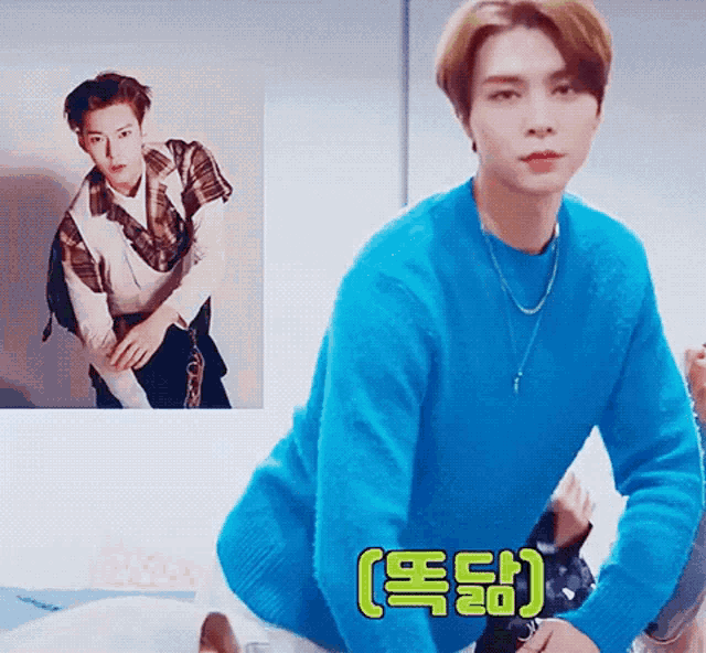 a young man in a blue sweater is sitting in front of a picture of himself