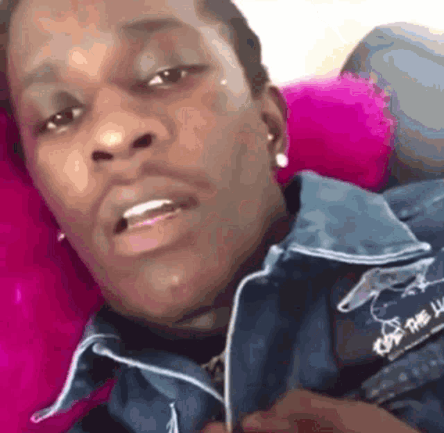 a man in a denim jacket is laying on a pink couch .