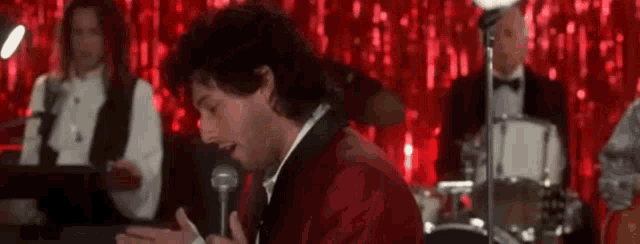 a man in a tuxedo is singing into a microphone while playing a piano .