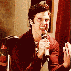 a man is singing into a microphone while wearing a red jacket .