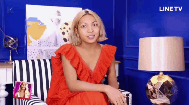 a woman in a red dress is sitting on a striped chair in front of a blue wall with line tv written on the bottom