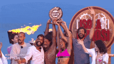 a group of people holding a trophy in front of a sign that says l' isola dei famosi