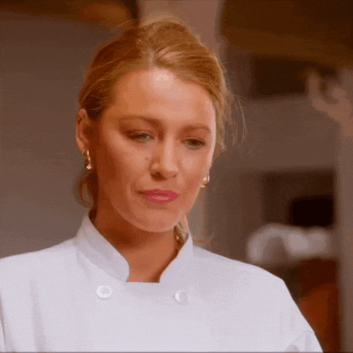 a woman wearing a white chef 's coat and earrings looks down