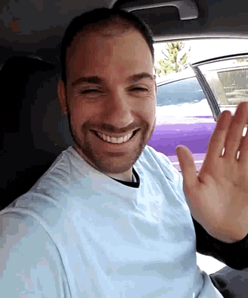 a man in a blue shirt is smiling and waving his hand