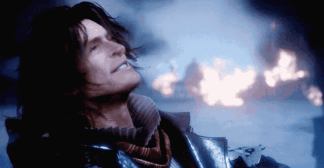 a man with long hair is smiling in front of a fire in the background