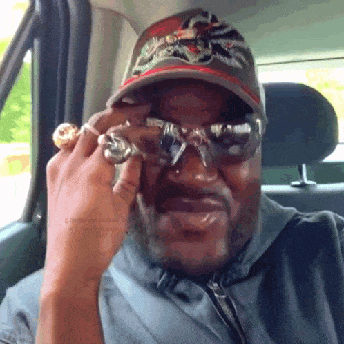 a man wearing a hat and sunglasses is sitting in the back seat of a car