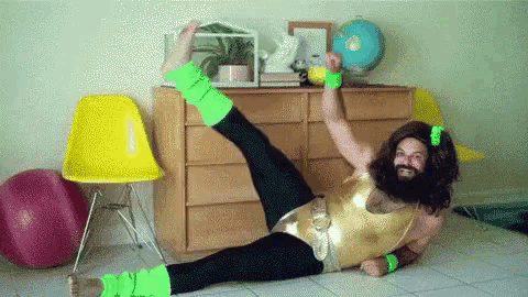 a man with a beard and neon green leg warmers is doing a split