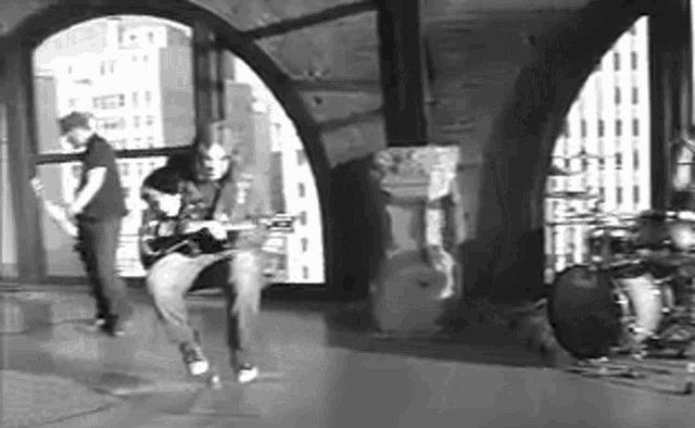 a black and white photo of a man playing a guitar and a drum set .