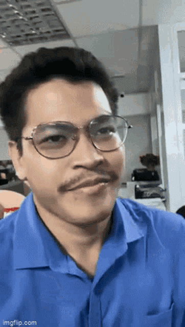 a man wearing glasses and a blue shirt with a mustache