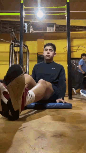 a man wearing a black under armour shirt sits on a blue mat in a gym