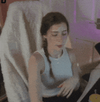 a woman in a white tank top is sitting in a chair with a braid